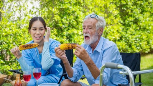 Caregiver and Elderly Man Eating Corn — Disability Support in Wollongong, NSW